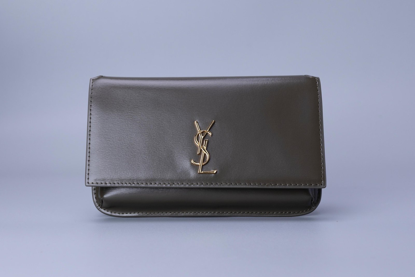 Bolsa compacta cinza-escura com aba frontal e detalhe metálico