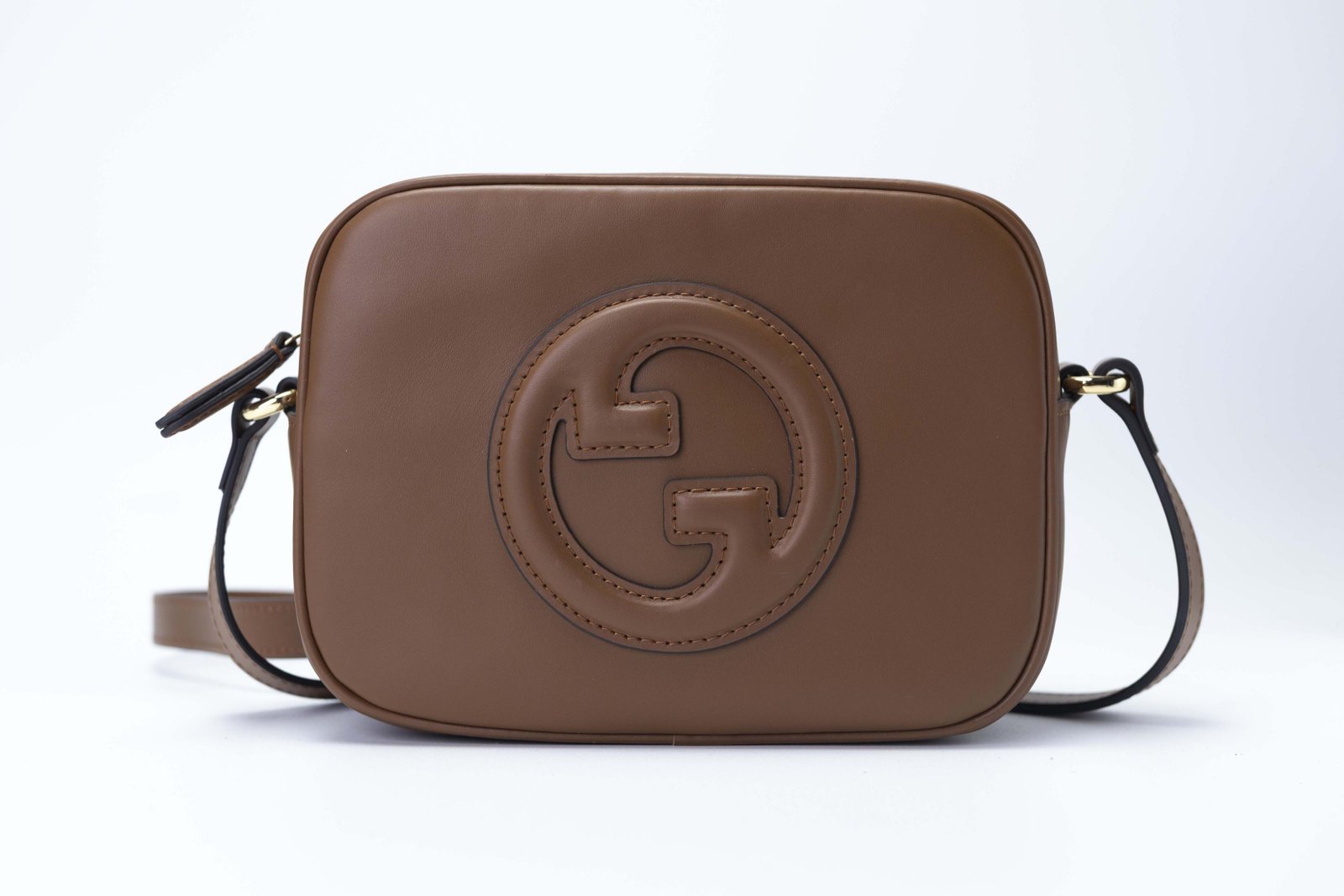 Bolsa marrom tiracolo com formato retangular e detalhe circular frontal
